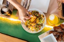 Зверху ростуть нерозпізнані самиці, які їдять смачні традиційні мексиканські начо з перцем джалапено з сиром і соусом гуакамоле, що сидять за столом у ресторані. — стокове фото