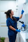 Side view of content female veterinarian in uniform with test tube standing at table with microscope in laboratory — Stock Photo