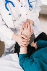 Зверху анонімний лікар, який розмовляє з літньою жінкою, тримаючись за руки під час огляду в лікарні — стокове фото