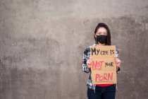 Этническая женщина в защитной маске, стоящая с плакатом My Life Is Not Your Carton во время защиты от сексуальных домогательств и нападений — стоковое фото