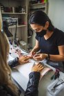 Master removing gel nail polish of female client with foil sitting at table in spa center — Stock Photo