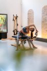 Konzentrierte, fitte Frau sitzt auf Bank und streckt Arme während des Trainings auf Pilates-Gerät — Stockfoto