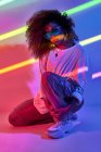 Ganzkörpermodisch selbstbewusste afroamerikanische Tänzerin mit lockigem Haar und Sonnenbrille steht im Neonlicht eines Tanzstudios — Stockfoto
