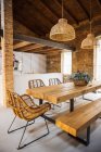Kitchen and dining room interior with wooden table and wicker armchairs under lamps against brick walls in light house — Fotografia de Stock