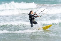 Athlète féminine active sur le kiteboard tenant la barre de contrôle tout en pratiquant le kitesurf et en regardant loin sur l'océan mousseux — Photo de stock