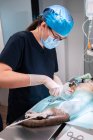 Female vet in mask and eyeglasses using medical scissors while operating feline patient on table in hospital — Stock Photo