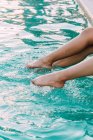 Crop anônimo descalço mulheres viajantes tocando brilhante ondulado água na piscina durante a viagem — Fotografia de Stock