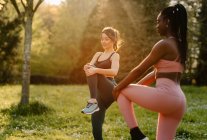 Junge multirassische Sportlerinnen in Sportbekleidung strecken an sonnigen Tagen die Beine auf dem asphaltierten Fußweg der Stadt — Stockfoto