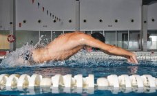 Vista laterale di un forte nuotatore maschio in cuffia da bagno che esegue un colpo di farfalla durante l'allenamento in piscina con acqua blu — Foto stock