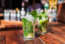 Bicchieri di rinfrescanti cocktail di mojito con ghiaccio e menta serviti sul bancone del bar all'aperto in legno — Foto stock