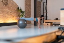 Seitenansicht einer fitten Frau in Sportbekleidung, die während des Trainings im Pilates-Studio auf einem fitten Ball trainiert — Stockfoto