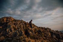 Seitliche Ansicht der Frau zu Fuß bergab auf felsigen Hang des Berges in grünem Tal mit bewölkten Sonnenuntergang Himmel auf dem Hintergrund — Stockfoto
