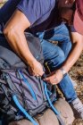 Высокий угол зрения человека в повседневной одежде, надевающего откормочный рюкзак во время походов на солнечной природе — стоковое фото