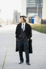 Auto-assegurada jovem empresário étnico masculino em terno formal e casaco de pé com as mãos nos bolsos enquanto olha para longe na cidade — Fotografia de Stock