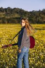 Jeune femme hipster réfléchie debout sur une prairie à la campagne écrivant des chansons sur ordinateur portable et jouant de la guitare pendant la lumière du soleil d'été en regardant la caméra — Photo de stock