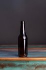 Garrafa de vidro escuro de bebida alcoólica em mesa de madeira pintada em forma quadrada em casa — Fotografia de Stock