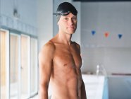 Masculino nadador masculino en gafas profesionales con el cuerpo muscular de pie antes del entrenamiento en la luz del sol sobre fondo borroso mirando a la cámara - foto de stock