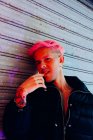 Homem homossexual jovem com tatuagem e cabelo rosa em outerwear elegante olhando para a câmera contra a parede resistida — Fotografia de Stock