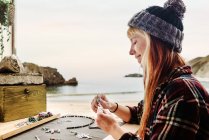 Seitenansicht von zufriedenen Reisenden, die handgefertigte Accessoires kreieren, während sie am Holztisch in einem geparkten LKW am Meer sitzen — Stockfoto