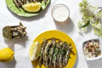 From above of delicious fried anchovies served on plates with lemon and placed on white table with glass of beer — Fotografia de Stock
