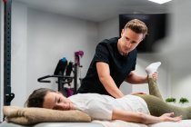 Дорослий фізіотерапевт торкається ноги жінки з закритими очима під час огляду на ліжку в лікарні — стокове фото