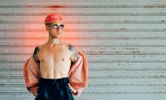 Junge Schwule mit moderner Sonnenbrille und stylischer Pelzjacke mit rosa Haaren gegen graue Wand — Stockfoto
