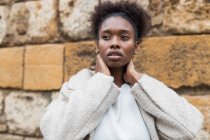 Portrait of attractive African American female with coat standing in historic city district on warm spring day and looking away — Stock Photo