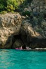 Vista lateral viajeros anónimos con remos flotando en agua de mar turquesa cerca de la costa rocosa en un día soleado en Málaga España - foto de stock