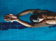 Vista superior do atleta masculino em touca de banho com braços levantados nadando na parte de trás na piscina durante o treinamento — Fotografia de Stock
