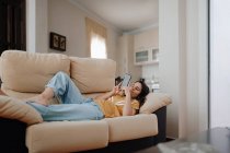 Вид сбоку молодой женщины, делающей автопортрет на мобильном телефоне, лежа на диване в гостиной — стоковое фото