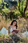 Dreamy charming brunette in white dress sitting on field meadow and reading book in sunlight — Stock Photo
