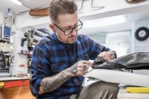 Artesanato barbudo criativo costura estofos de couro para assento de moto enquanto trabalhava na oficina — Fotografia de Stock