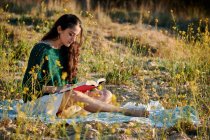 Dreamy charming brunette in white dress sitting on field meadow and reading book in sunlight — Photo de stock