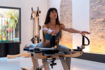 Concentrado ajuste feminino alongamento pernas e fazendo exercícios lunge em pilates reformador durante o treinamento em ginásio — Fotografia de Stock