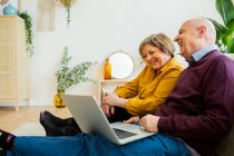 Alegre pareja madura hablando en video chat en el ordenador portátil en la sala de estar - foto de stock