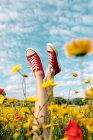 Colheita fêmea irreconhecível em calçado brilhante deitado com pernas cruzadas entre margaridas florescentes sob céu azul nublado no campo — Fotografia de Stock