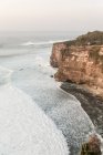Ruvida scogliera rocciosa bagnata da un mare ondulato e schiumoso sotto un cielo blu senza nuvole in una natura panoramica — Foto stock