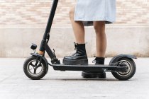 Cropped unrecognizable female in casual wear riding scooter on paved sidewalk - foto de stock