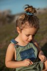 Delighted adorable little girl in overalls standing in meadow and looking down — Stock Photo