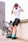 Bearded male bicyclist in modern sunglasses and sportswear against urban building under white sky in daytime — Fotografia de Stock