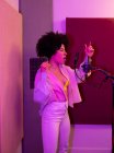 Cantora negra cantando música contra microfone com filtro pop enquanto está de pé com a mão no quadril e olhos fechados no estúdio de som — Fotografia de Stock