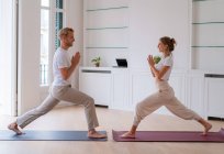 Side view of content couple in activewear standing on mats in Anjaneyasana with Namaste gesture while doing yoga in morning and looking at each other — Fotografia de Stock