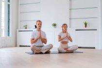 Peaceful couple sitting in Lotus pose with prayer hands while practicing yoga together and meditating with closed eyes — Stock Photo
