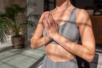 Ritaglia femmina irriconoscibile con le mani di preghiera meditando in camera con la luce del sole mentre pratichi yoga a casa — Foto stock