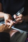Crop unrecognizable female master using electric nail file while doing manicure for client in beauty salon — Stock Photo