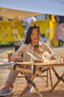 Азиатская девушка просматривает мобильный телефон, отдыхая сидя за столом в кемпинге — стоковое фото