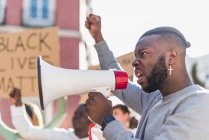 Side view of African American male screaming in megaphone during Black Lives Matter protest in city while standing in crowd of multiethnic demonstrators — Fotografia de Stock