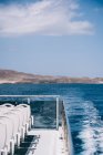 Порожні білі стільці на палубі круїзного човна, що пливе у блакитній морській воді з горою на березі — стокове фото