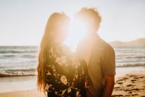 Hombre abrazando joven novia atractiva en traje de baño mientras se enfrían juntos en la costa arenosa cerca de acantilados ásperos en el día soleado en Fyriplaka Milos - foto de stock
