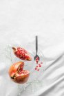 Bright tasty fresh pomegranate with ripe seeds and blooming flower sprig on transparent stand on crumpled fabric — Stock Photo